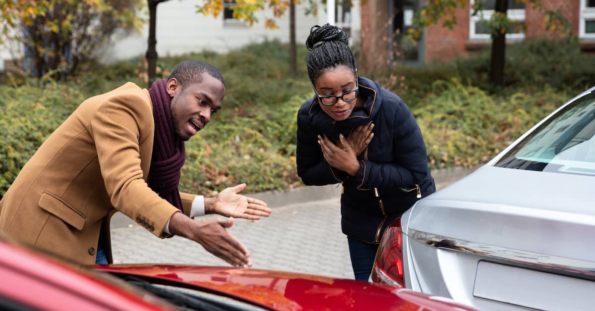 Two people assess damage to two cars after a fender bender.